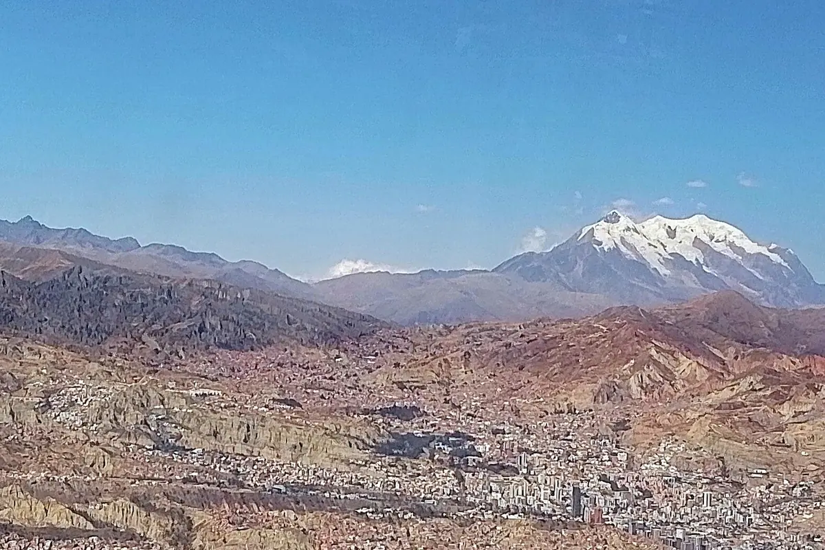 The valley of La Paz seen from a cable car, with brown hills and buildings below and snow-capped peaks of the Cordillera Real on the horizon